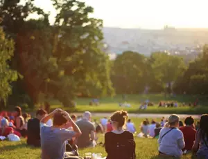 Foule assise dans un champs, entourés d'arbres, faisant face au soleil couchant