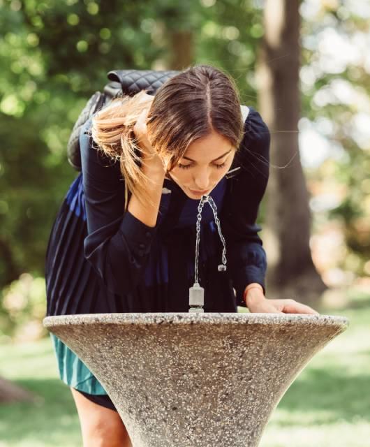 Femme buvant à une fontaine à eau dans un parc