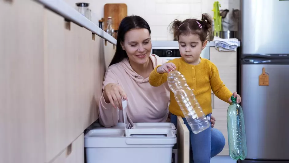 Mère avec son enfant recyclant des bouteilles en plastique dans une cuisine